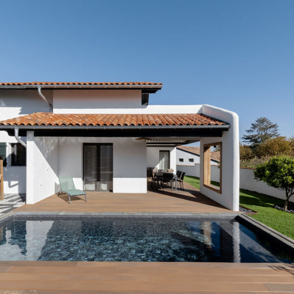 Vue d’une maison contemporaine familiale avec grandes baies vitrées, cuisine ouverte et salle à manger lumineuse donnant sur jardin et piscine.