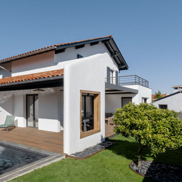 Vue d’une maison contemporaine familiale avec grandes baies vitrées, cuisine ouverte et salle à manger lumineuse donnant sur jardin et piscine.
