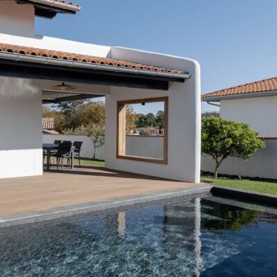 Vue d’une maison contemporaine familiale avec grandes baies vitrées, cuisine ouverte et salle à manger lumineuse donnant sur jardin et piscine.