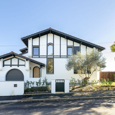 Vue d’une maison contemporaine familiale avec grandes baies vitrées, cuisine ouverte et salle à manger lumineuse donnant sur jardin et piscine.